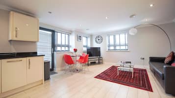A modern living room with a sofa, a dining area with red chairs, a TV, and a large clock on the wall.