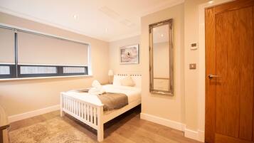 A bedroom with a white bed, a large mirror, a wooden door, and a window with blinds.