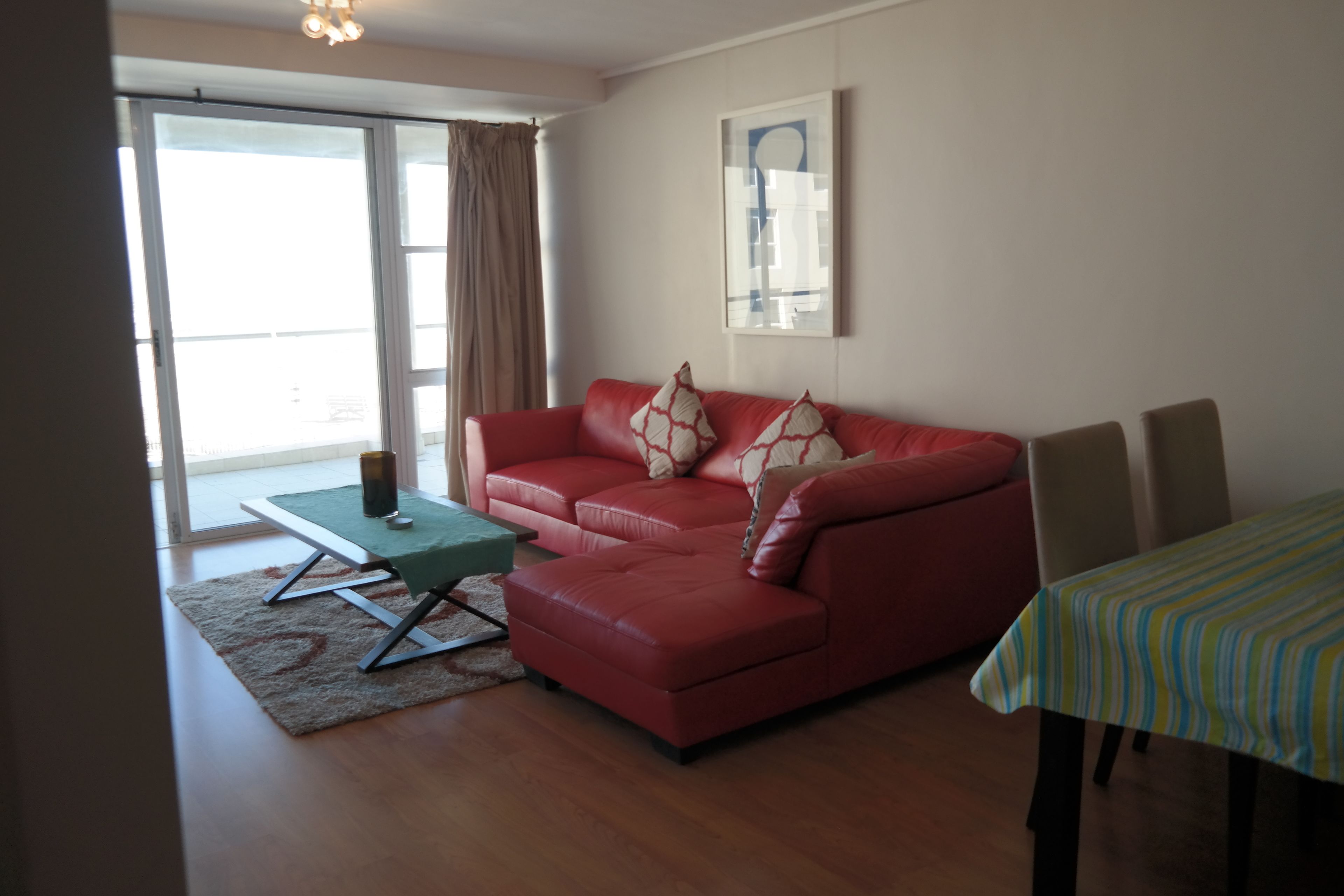A living room with a red sofa, a small table, and a dining area with a striped tablecloth.