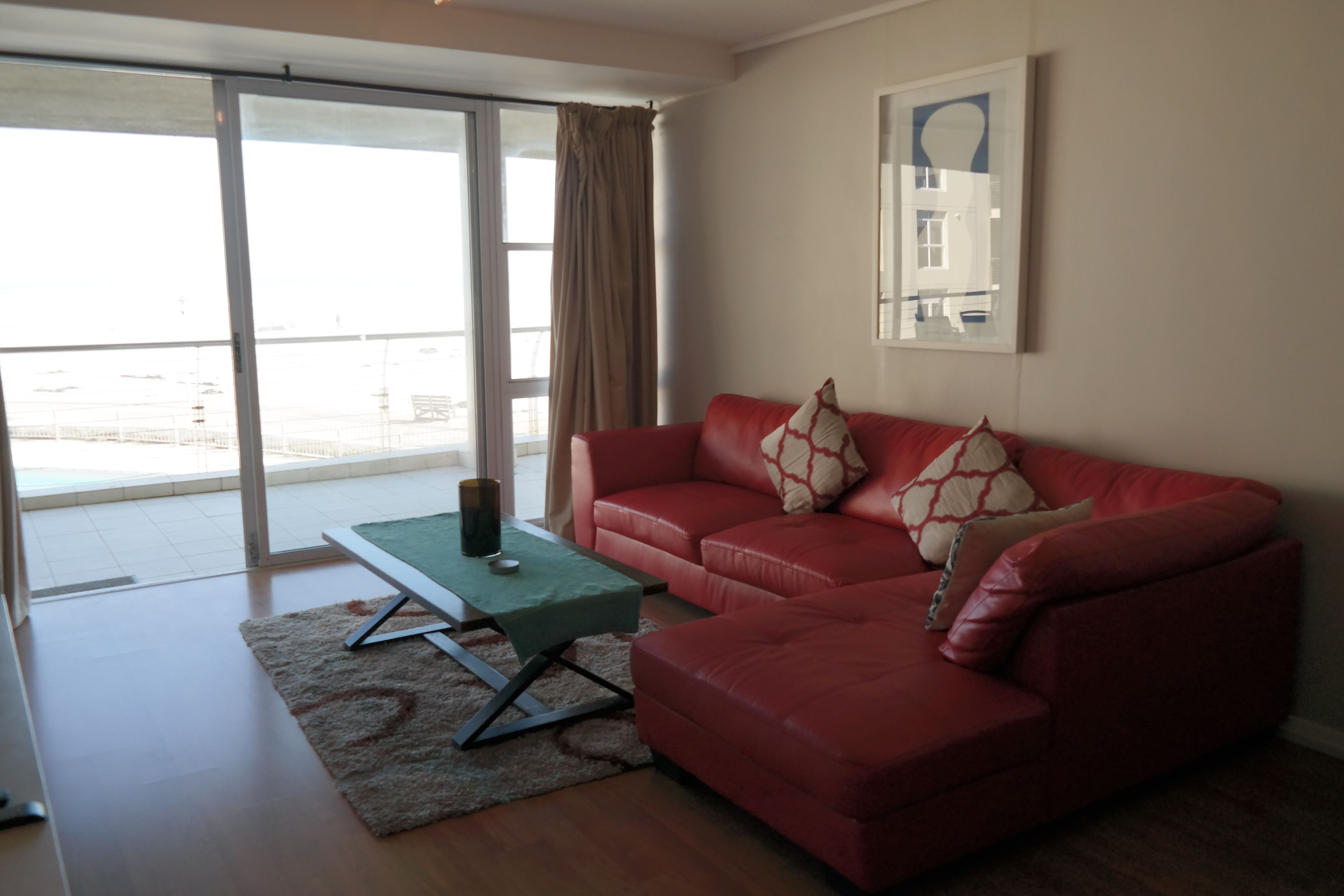 A living room with a red leather sofa, a green coffee table, and a large window with a view of a building.