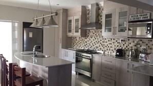 A modern kitchen with a central island, stainless steel appliances, and a sign that reads "NEVER TRUST A SKINNY COOK". - Clairwood Villa (Cape Town)