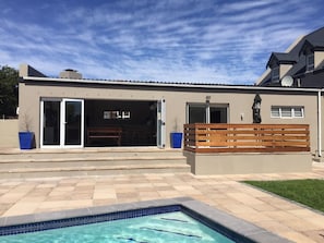 A modern house with a swimming pool, a patio with a wooden bench, and a garage door open.