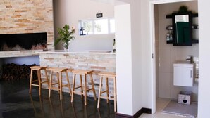 A kitchen with a stone backsplash, wooden stools, and a window. - Clairwood Villa (Cape Town)