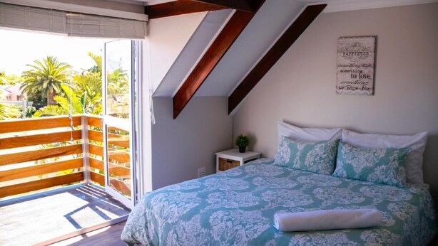 A bedroom with a bed, a nightstand, a window, and a balcony. - Clairwood Villa (Cape Town)