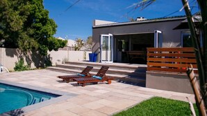 A modern outdoor pool area with a clear blue sky, a pool, and two sun loungers. - Clairwood Villa (Cape Town)