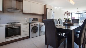 A modern kitchen with built-in appliances, a dining area with chairs, and a view through large windows. - Quayside 301 by CTHA (Cape Town)