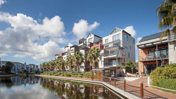 A modern residential building with balconies, a reflective water body, and palm trees. - Quayside 301 by CTHA (Cape Town)