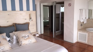 A hotel room with a bed, a wooden headboard, a bathroom with a sink and mirror, and a sliding glass door leading to a balcony.
