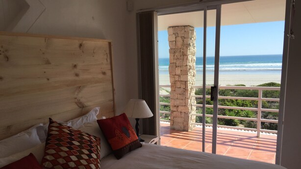A hotel room with a large bed, a wooden headboard, and a view of the ocean through a glass door.