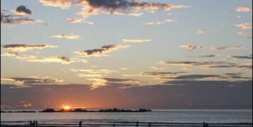 Un atardecer sobre un mar tranquilo con una masa de tierra a lo lejos.