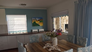 A dining area with a wooden table, patterned chairs, a vase of flowers, and a painting on the wall.