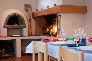 Un comedor con chimenea de ladrillo, sillas de madera y una mesa para dos, con copas de vino y platos.