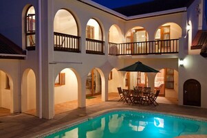 Zona junto a la piscina con mesa y sillas, rodeada de arcos y un balcón.