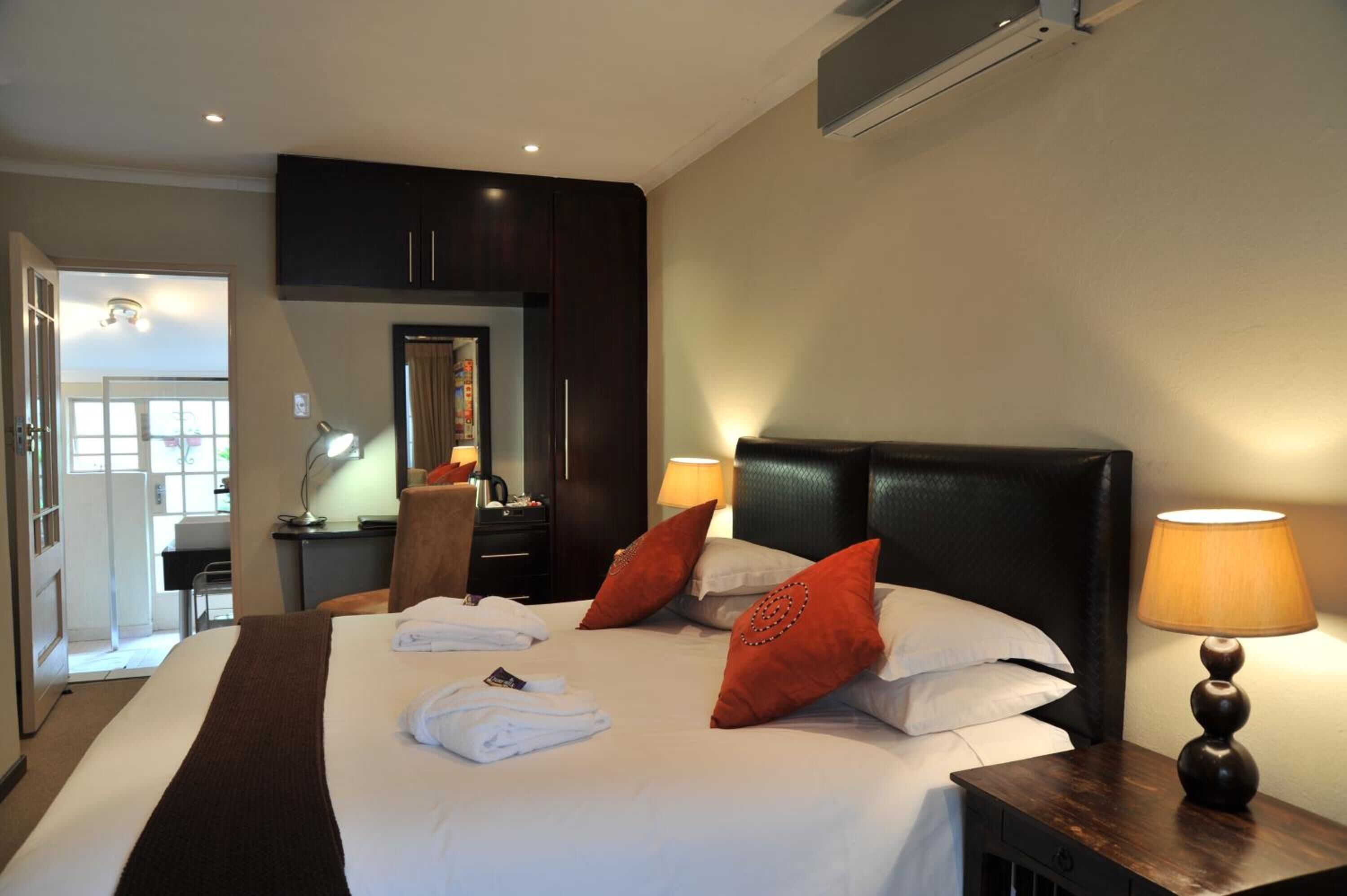 Hotelkamer met een groot bed, twee kussens, een nachtkastje met een lamp, een bureau met een stoel, en een kledingkast.