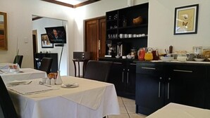 A dining area with tables set for meals, a kitchen with dark cabinets, and a framed picture on the wall. - Sand River Guest House (Sandton)