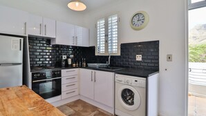Cocina compacta con armarios blancos, encimera negra, horno integrado, lavadora y un amplio ventanal.
