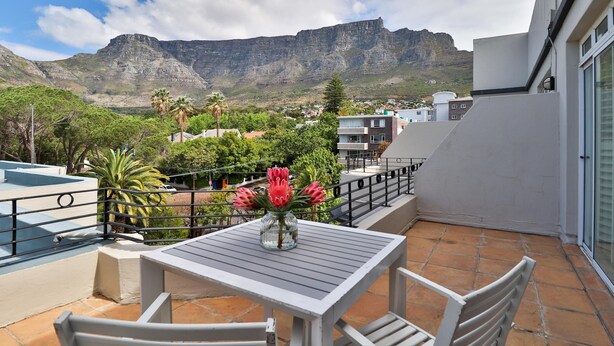 Una terraza con una mesa y sillas, un florero con flores y vistas a una montaña y pueblo.