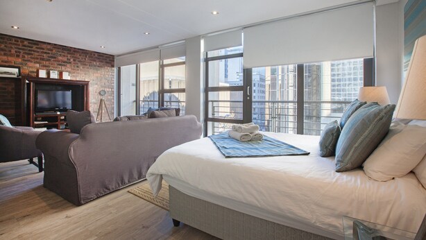 Une chambre d’hôtel moderne avec un grand lit, un canapé, une télévision et un mur en briques.