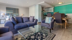 Un salon moderne avec une table basse en verre, un canapé et un coin repas comprenant une table et des chaises en bois.