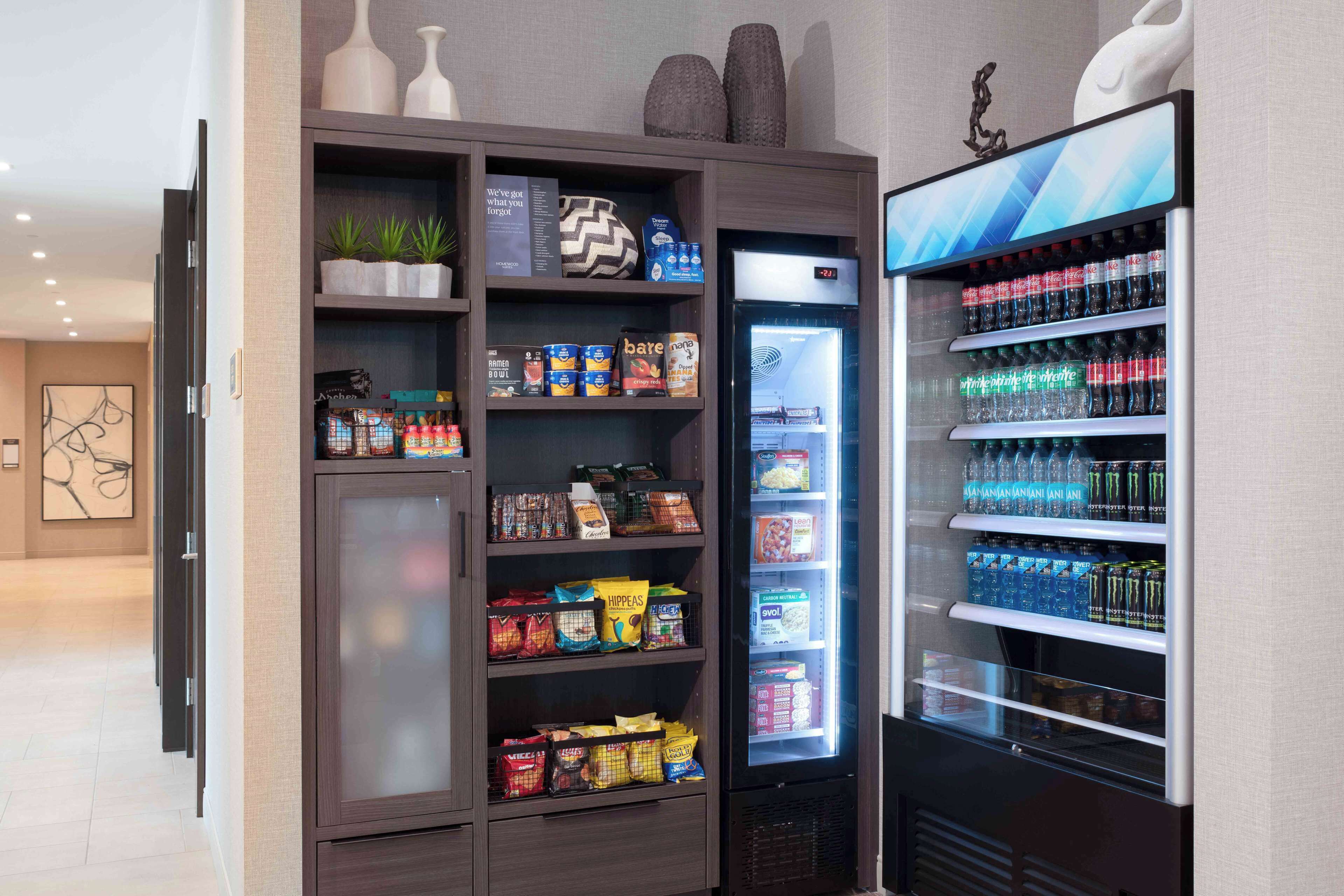 Una kitchenette con un refrigerador lleno de bebidas y aperitivos, un microondas y un armario con diferentes alimentos.