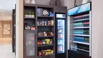 Una kitchenette con un refrigerador lleno de bebidas y aperitivos, un microondas y un armario con diferentes alimentos.