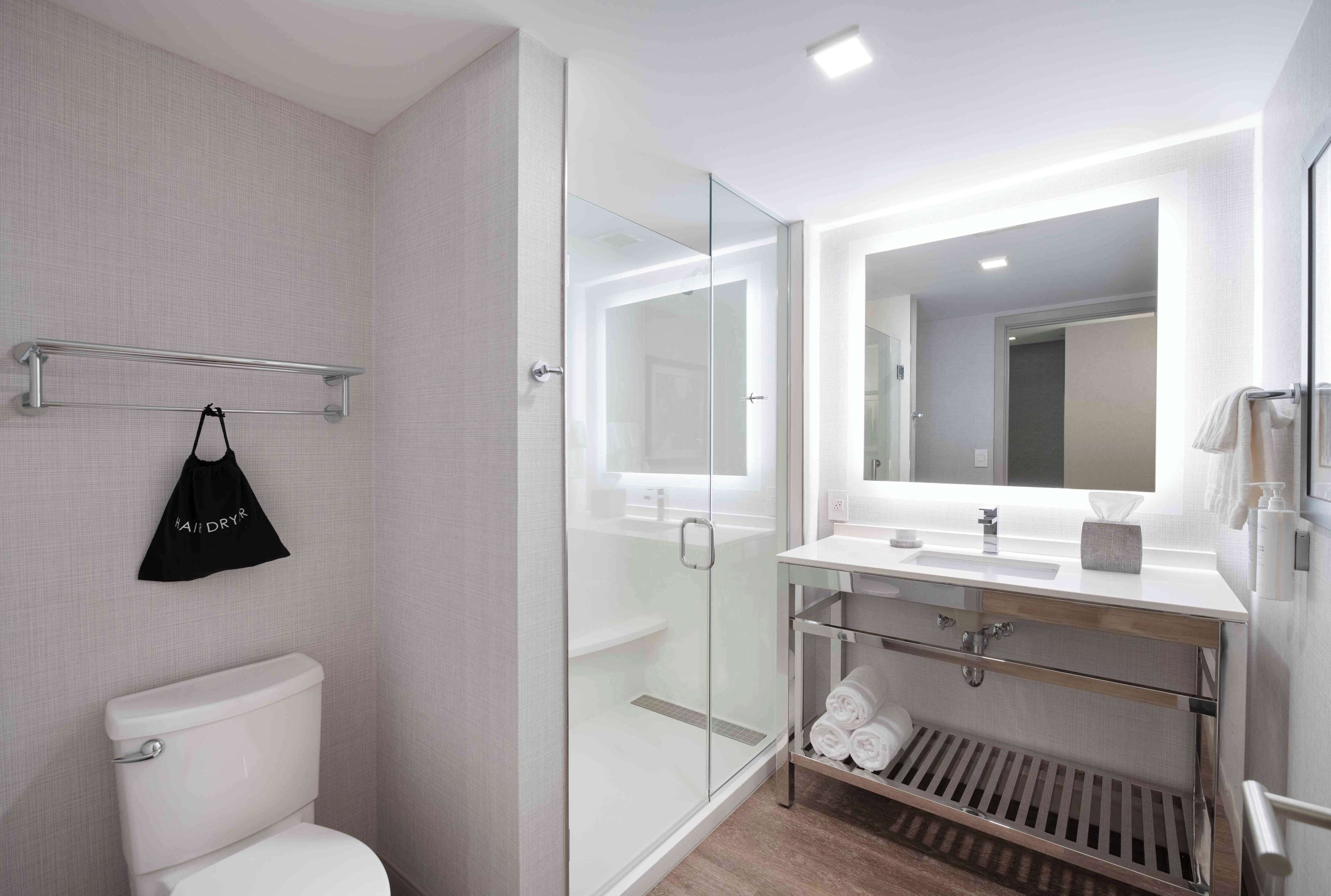 Et moderne badeværelse med brusekabine i glas, toilet i hvidt, vaskebord med spejl og et håndklædetørrestativ.
