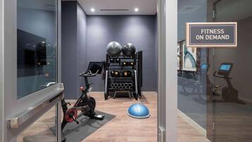 Espaço fitness com equipamentos de exercício, incluindo uma bicicleta ergométrica, suporte para pesos e bolas de exercício.