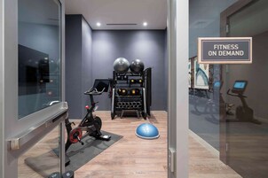 Espaço fitness com equipamentos de exercício, incluindo uma bicicleta ergométrica, suporte para pesos e bolas de exercício.