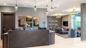 A modern hotel reception area with a curved reception desk, framed artwork, and a seating area with sofas and a coffee table. - Homewood Suites by Hilton Boston Logan Airport Chelsea (Chelsea)