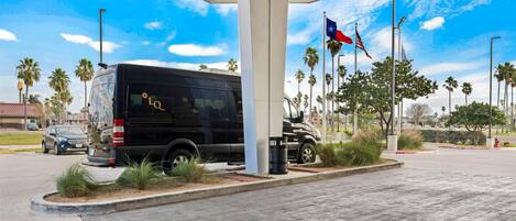 A parking area with a black SUV, palm trees, and flags.