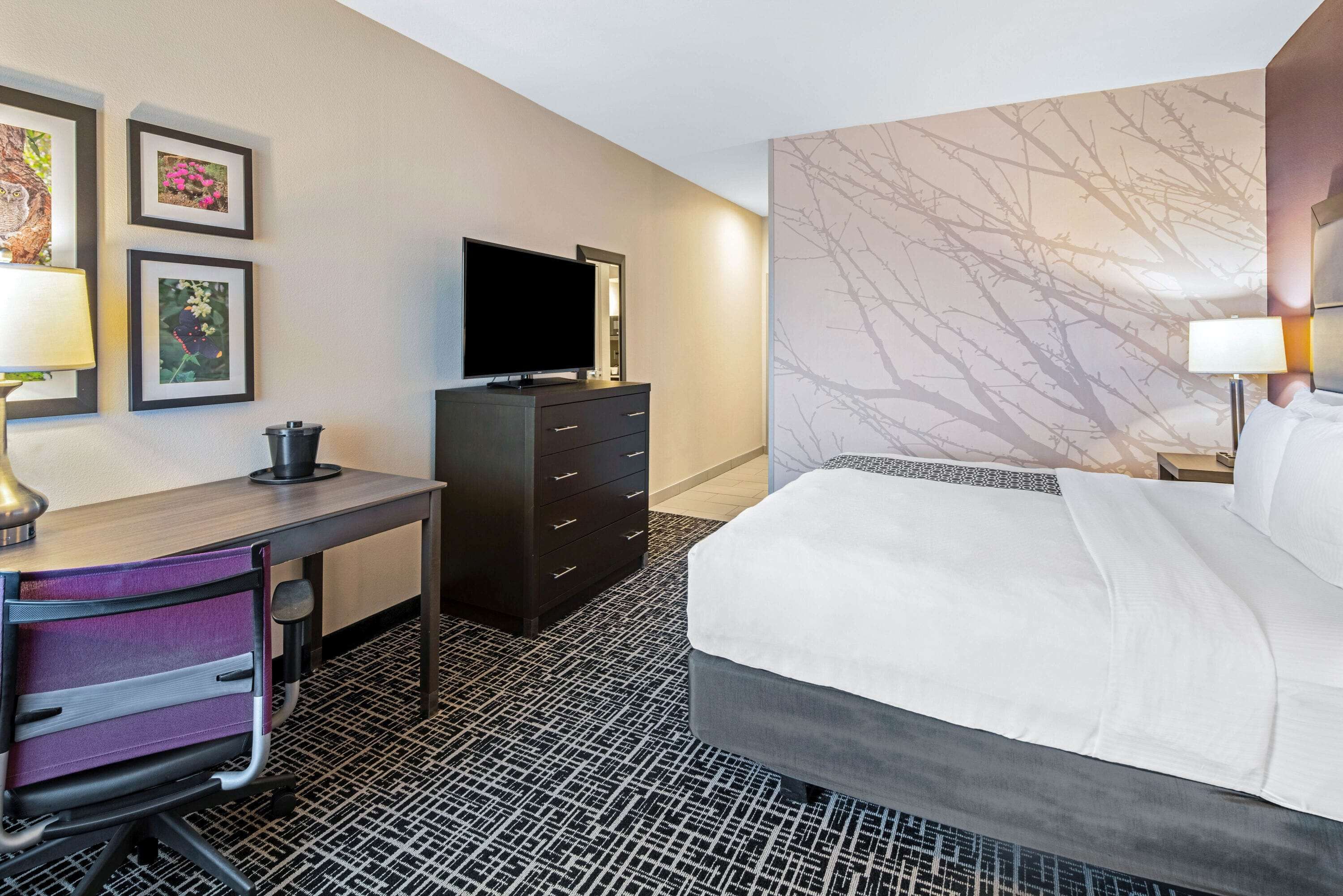 A hotel room with a bed, a desk with a computer, a TV, and a dresser.