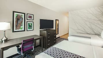 Une chambre d’hôtel équipée d’un bureau, d’une chaise, d’une télévision, d’une commode et d’un lit avec une literie à motifs.