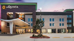 Hotel La Quinta con fachada moderna, un acceso cubierto y una zona ajardinada con un árbol.