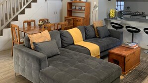 A spacious living room with a large sectional sofa, a wooden dining table, and a staircase. - La Gratitude Guest House (Franschhoek)
