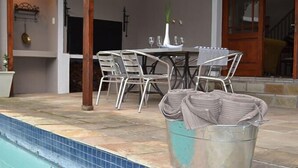 A swimming pool with a tiled deck, a table with chairs, and a potted plant. - La Gratitude Guest House (Franschhoek)