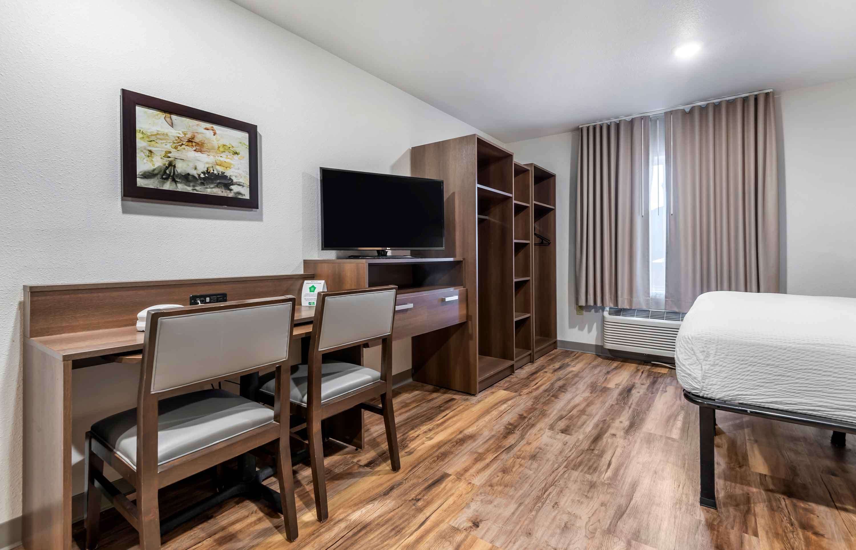 A hotel room with a wooden desk, a television, a bed, and a large window with curtains.