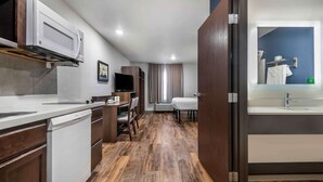 A modern hotel room with a kitchen area, a dining table, and a bathroom with a mirror and sink. - Extended Stay America Select Suites - Pittsburgh - Cranberry (Cranberry Township)