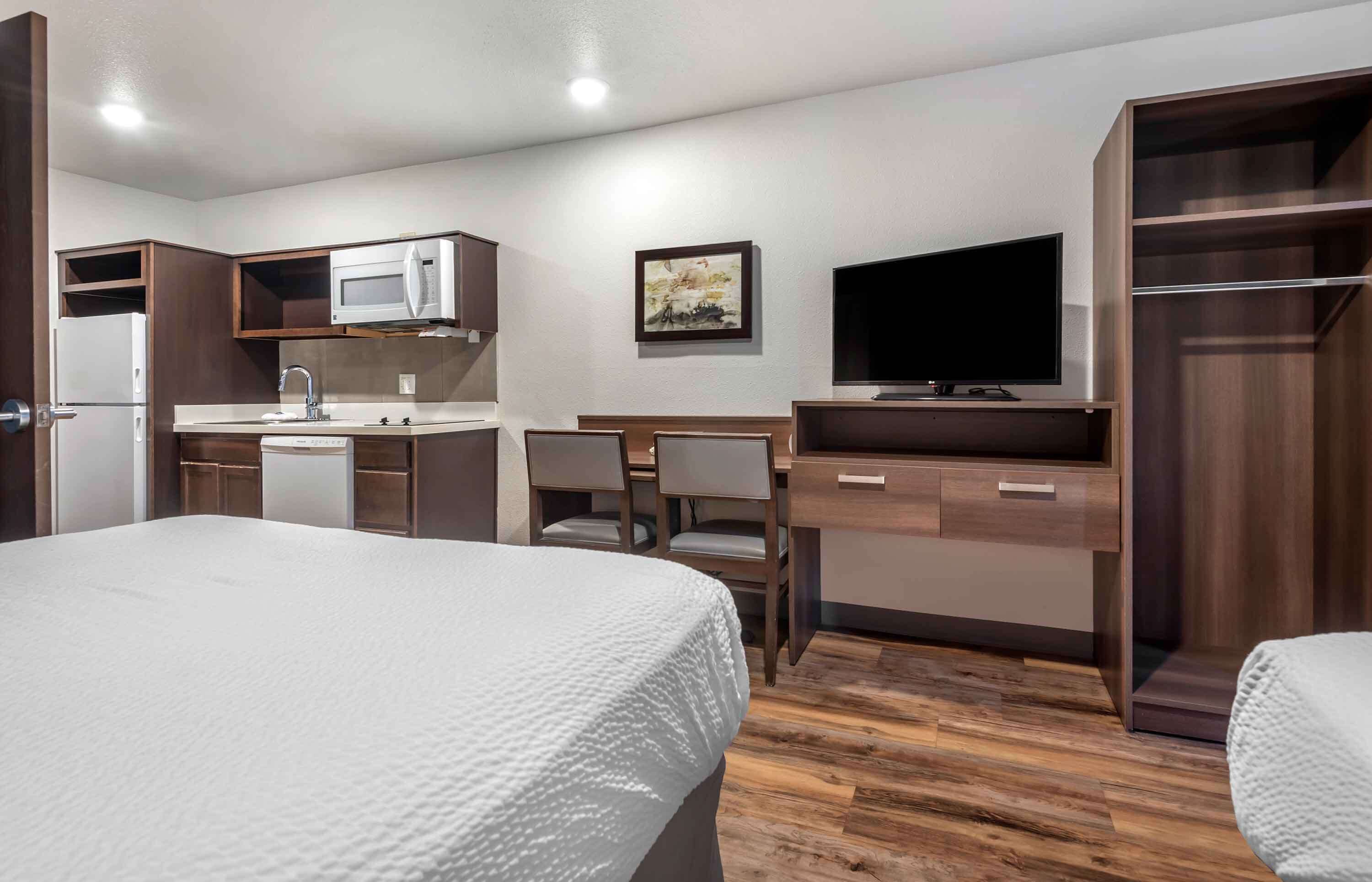 Habitación de hotel con una cama, un escritorio con silla, microondas, lavabo, televisor y armario.