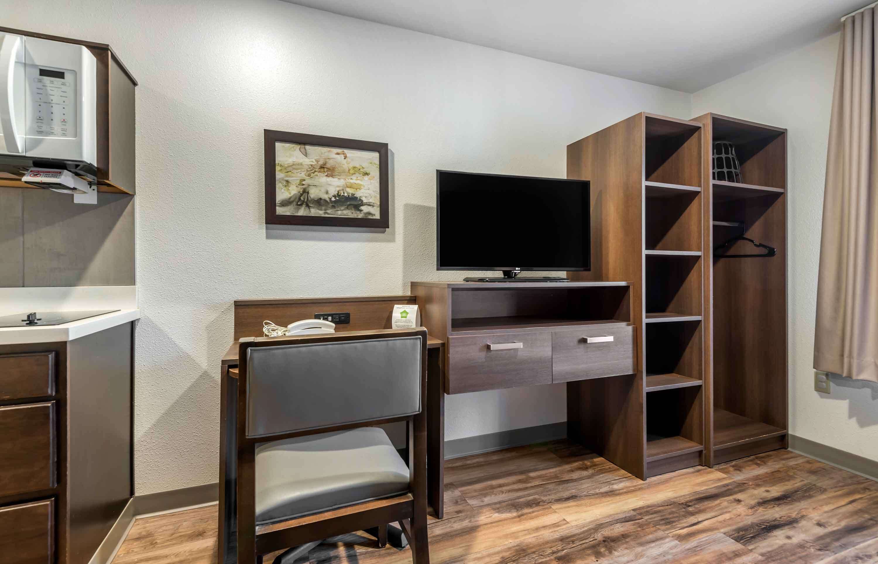 A hotel room with a wooden desk, a television, a wardrobe, and a small seating area.