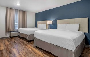 Habitación de hotel con dos camas, una ventana con cortinas, un calentador y una pared azul.