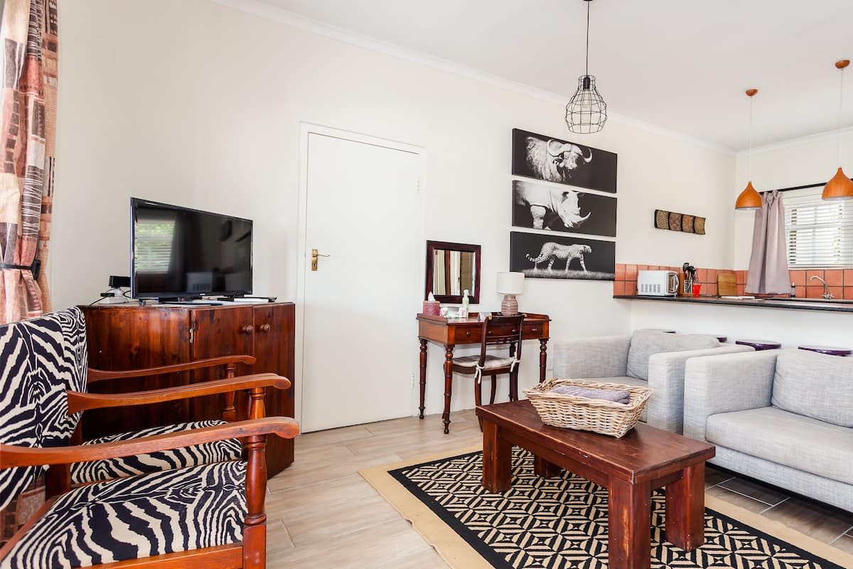 Una sala de estar con un sofá, un mueble de madera, un televisor, una mesa de comedor con sillas y una zona de cocina con ventana.