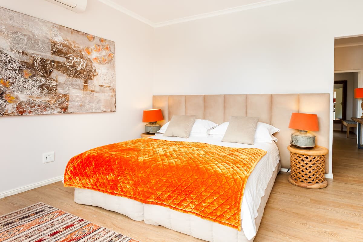 Un dormitorio con una cama grande, dos mesitas de noche con lámparas, suelo de madera y un cuadro en la pared.