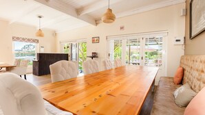 A spacious dining area with a wooden table and white upholstered chairs, large windows with a view of greenery, and a cozy seating area with a cushioned sofa. - Lady Loch Country House (Wellington)
