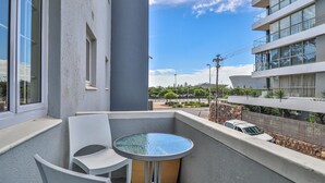 A balcony with a round table and two chairs, overlooking a street with a modern building and parked cars. - Eaton Square 2 by CTHA (Cape Town)