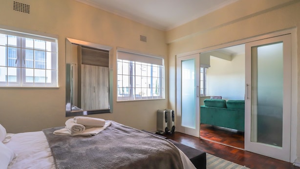 A bedroom with a bed, a radiator, a window, and a sliding glass door leading to a balcony. - Eaton Square 2 by CTHA (Cape Town)