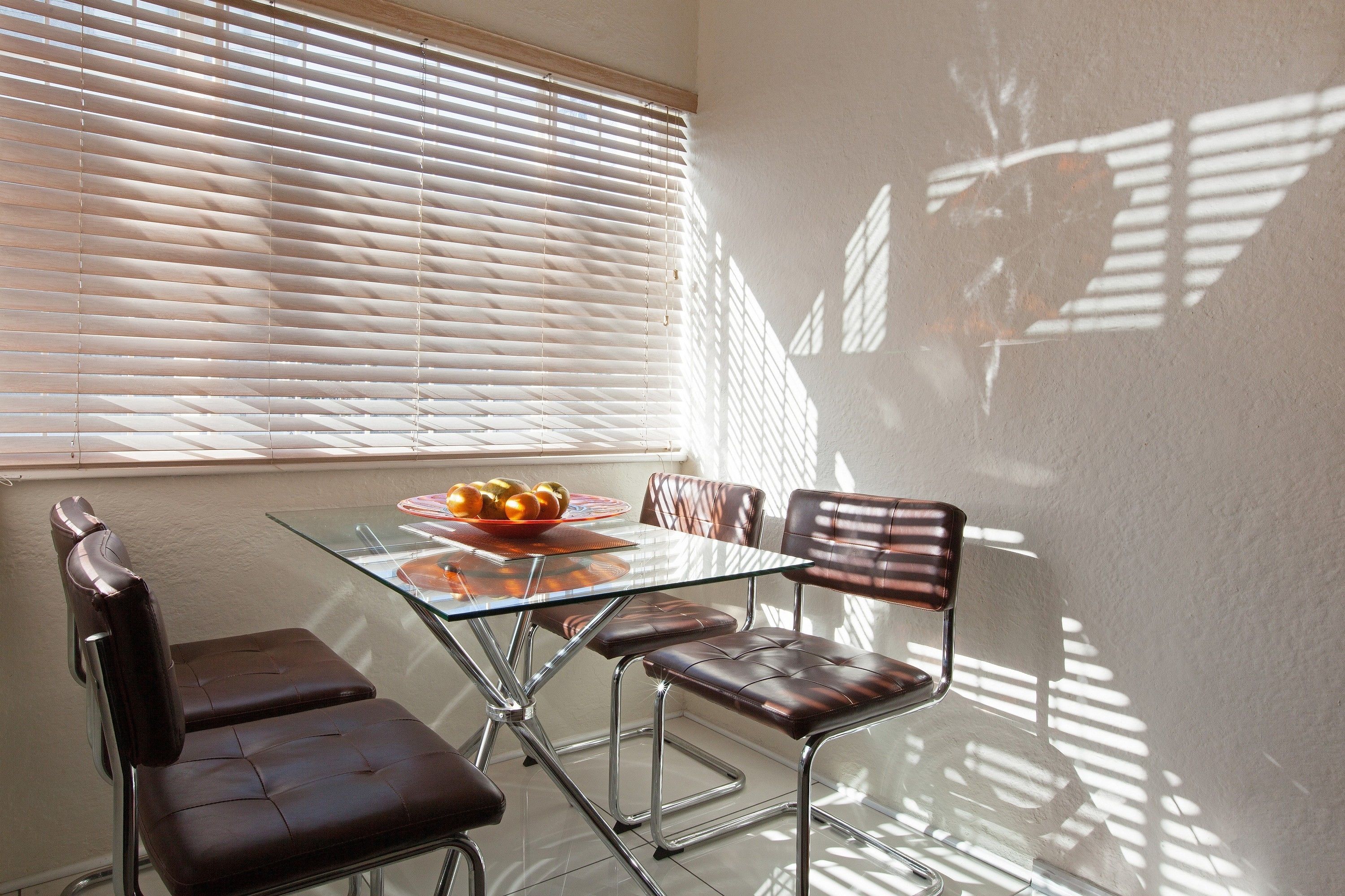 A dining area with a glass table, leather chairs, and a bowl of fruit on the table.