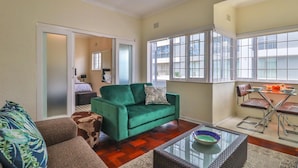 A living room with a green sofa, a brown sofa, a glass coffee table, and a dining area with a table and chairs. - Eaton Square 2 by CTHA (Cape Town)