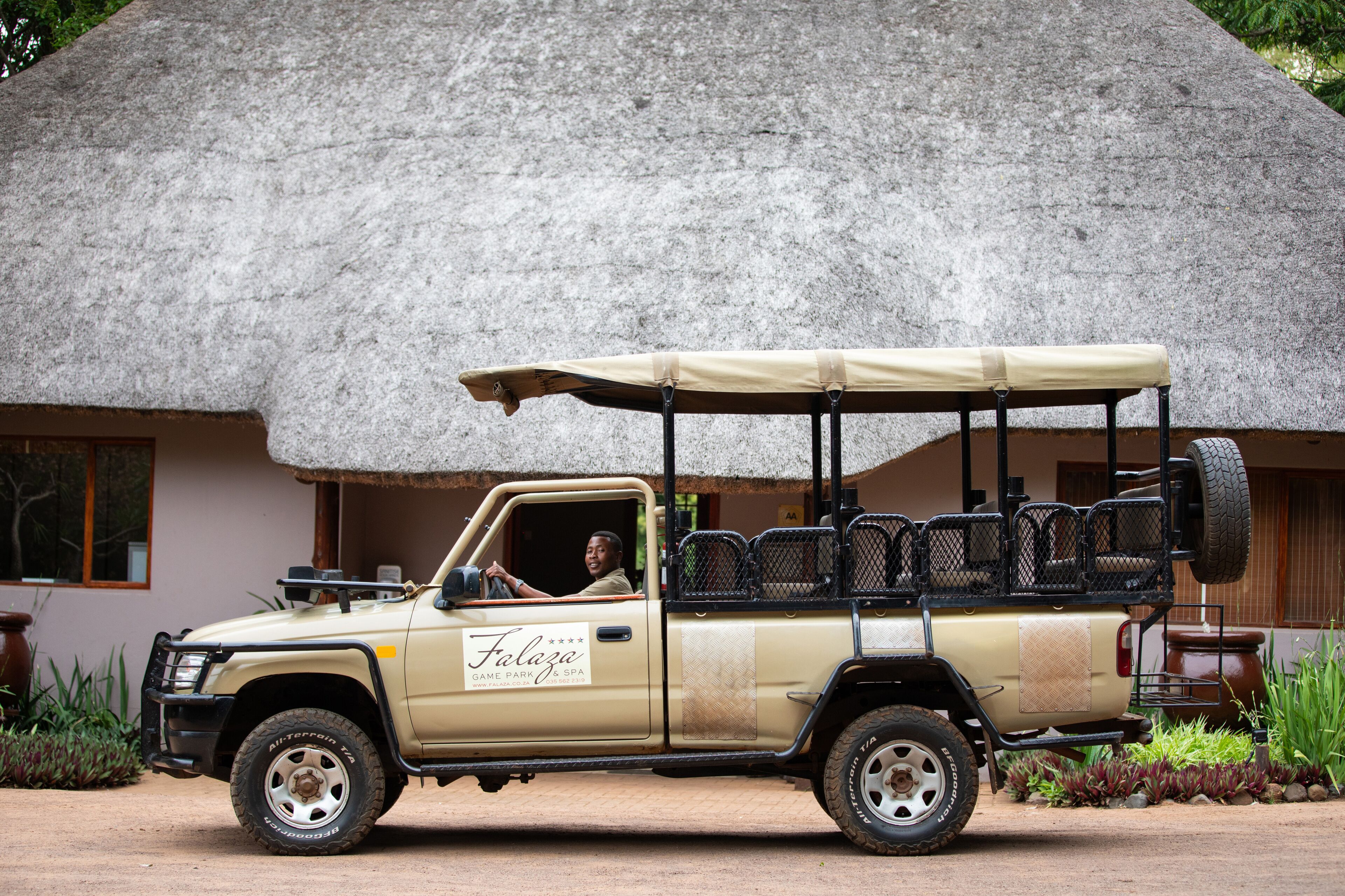 A beige safari vehicle parked in front of a building with a thatched roof.