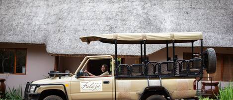 A beige safari vehicle parked in front of a building with a thatched roof.
