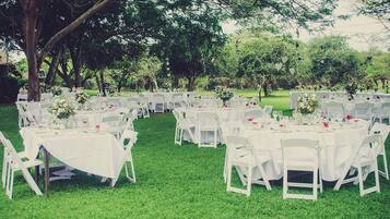 An outdoor wedding venue with multiple round tables covered with white tablecloths, surrounded by white chairs.